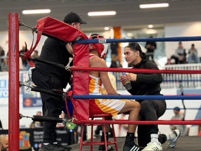Coach Dev speaking with a boxer in red headgear between rounds.